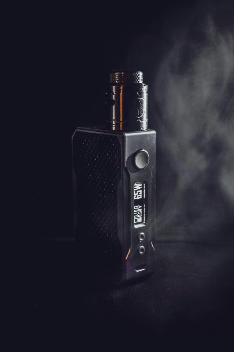 Dark and atmospheric close-up of a vape mod with subtle smoke in the background.