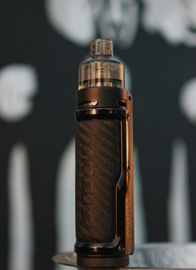 Stylish vape pen with carbon fiber pattern against blurred abstract background.